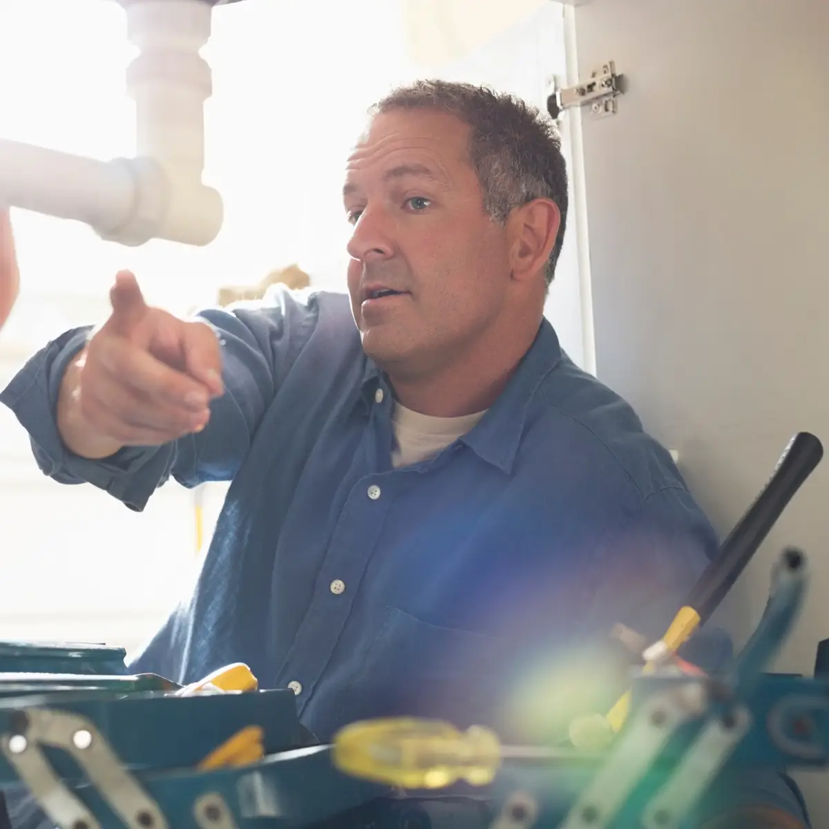 Residential-page-content-R@2x chinook plumbing plumber inspecting a pipe underneath a sink surrounded by plumbing tools